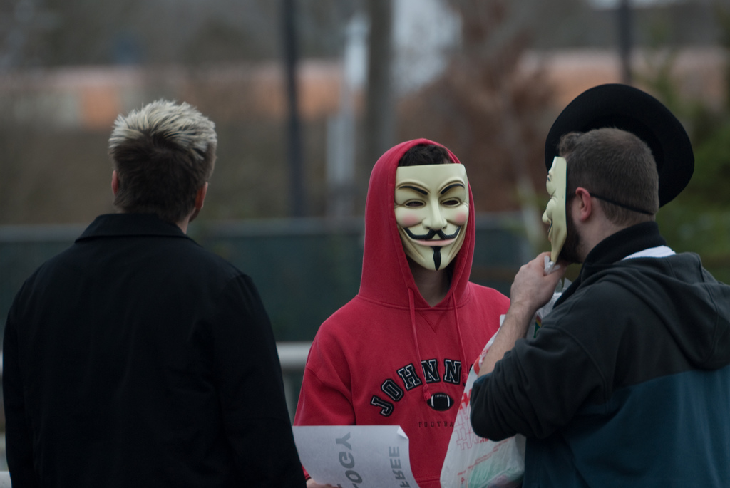 Anonymous protesters adjust their masks (image via Matt Westervelt)